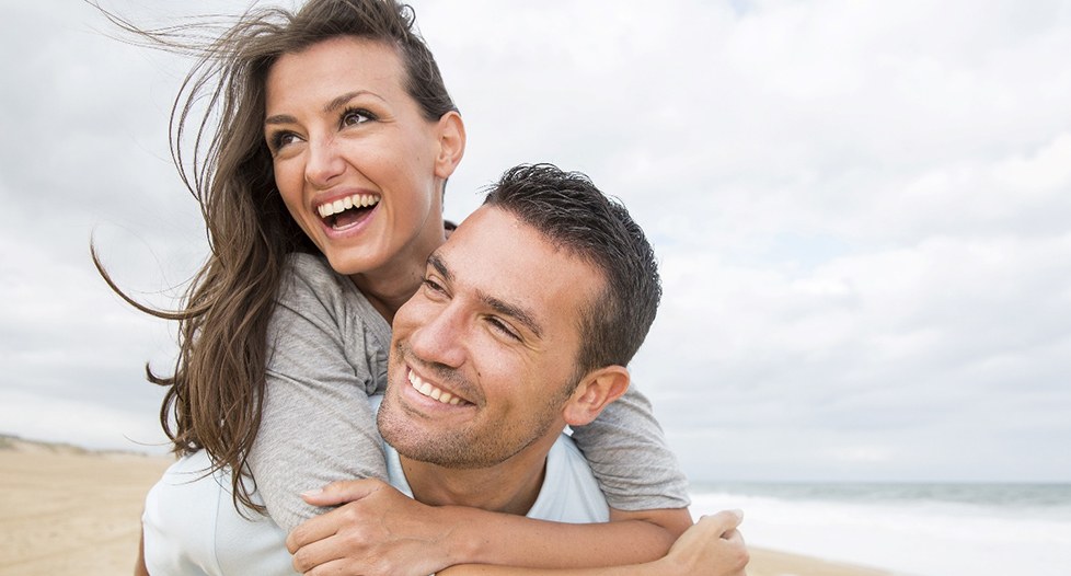 A young man and woman laughing and playing while on the beach after seeing their Aetna dentist in Park City