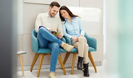 A man and woman wait in the lobby of a dentist’s office looking through a magazine