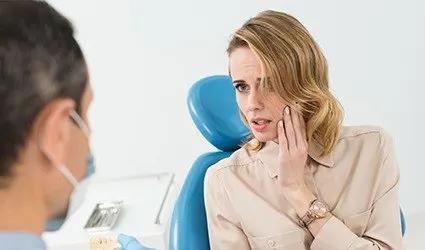 Woman in dental chair holding jaw