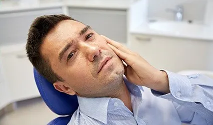 Man in dental chair holding jaw