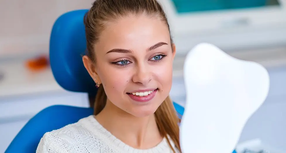 Woman in dental chair looking at smile in mirror