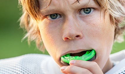 Teen placing green athletic mouthguard