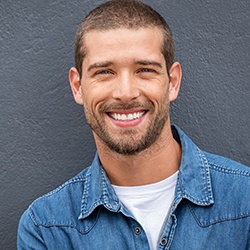 A young man wearing a denim button-down shirt and smiling after receiving his dental implants