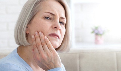 Older woman rubbing jaw due to dental implant pain